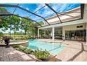 Enclosed pool area featuring a screened enclosure, adjacent spa, brick patio, and view of backyard and lake at 9630 Tree Tops Lake Rd, Tampa, FL 33626