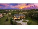 Aerial view of a luxurious lakeside home featuring manicured grounds, circular drive, and mature trees at sunset at 10614 Low Oak Terrace, Thonotosassa, FL 33592