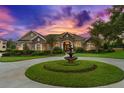 Beautiful home showcasing a circular driveway with a fountain, lush landscaping, and stone accents under a gorgeous sky at 10614 Low Oak Terrace, Thonotosassa, FL 33592