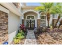 Inviting entrance with double doors, stone pillars, and lush landscaping creating a welcoming atmosphere at 12712 Stanwyck Cir, Tampa, FL 33626