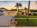 Charming home featuring a three-car garage, palm trees, manicured lawn, and warm exterior lights creating inviting curb appeal at 10213 Lockwood Pines Ln, Tampa, FL 33635