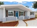 Inviting front porch with stone pillars, rustic shutters, and a vibrant blue front door at 1427 Gerard Ln, Holiday, FL 34690