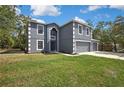 Charming gray two-story house showcasing a well-manicured lawn and large driveway with an attached two-car garage at 11257 Persimmon Ave, Weeki Wachee, FL 34614