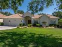 Charming single-story home featuring a well-manicured lawn, lush landscaping, and a tile roof at 12902 Grand Traverse Dr, Dade City, FL 33525