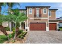 Two-story home with a brick driveway, palm trees, a two-car garage, and an iron-wrought Juliette balcony at 4419 Ortona Ln, Wesley Chapel, FL 33543