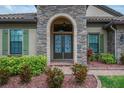 Close up of impressive stone-accented entryway with decorative glass door, and manicured shrubs at 803 Floresta St, Brandon, FL 33511