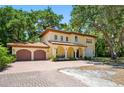 Charming Mediterranean-style home with a two-car garage and a brick driveway, set amidst mature trees at 1966 Freedom Dr, Clearwater, FL 33755