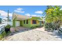 Exterior of the charming green home with red shutters and a covered carport, surrounded by lush greenery under a blue sky at 121 86Th Ter, Treasure Island, FL 33706