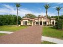 Beautiful Mediterranean-style home with a brick driveway, lush lawn, and towering palm trees on a sunny day at 2680 Keystone Springs Rd, Tarpon Springs, FL 34688