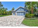 The blue house features a three-car garage, stone accents, lush landscaping, and a paver driveway at 14727 Tudor Chase Dr, Tampa, FL 33626