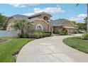 A tan two-story home featuring a curved driveway, an arched entryway, and a three-car garage, with mature landscaping at 16910 Equestrian Trl, Odessa, FL 33556