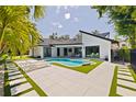 Modern backyard with a uniquely shaped pool, elegant lounge chairs, and pristine white tiling with grass accents at 7108 Pelican Island Dr, Tampa, FL 33634