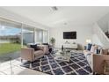 Bright living room featuring neutral furnishings, a textured rug, and large windows with views of the backyard and lake at 3488 Great Banyan Way, Wesley Chapel, FL 33543