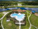 Stunning aerial view of a community pool, clubhouse, and lush landscaping by a pond at 16313 Treasure Point Dr, Wimauma, FL 33598