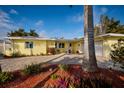 Charming single-story yellow home featuring a brick driveway, lush landscaping, and an attached two-car garage at 2487 W Bay Isle Se Dr, St Petersburg, FL 33705