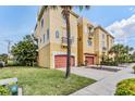 Stylish three-story condo featuring a terracotta garage door, balcony, and well-manicured lawn with palms at 6404 Mayra Shores Ln, Apollo Beach, FL 33572