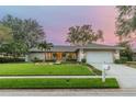 Inviting single-story home featuring lush front yard, mature trees, landscape lighting, and a wide driveway at 607 Grovewood Ln, Largo, FL 33770