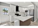 Bright kitchen featuring white cabinetry, stainless steel appliances, a black range hood, and a center island at 1235 Stockton Dr, Clearwater, FL 33755