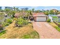 Single-story home with a red brick driveway, attached garage, and lush tropical landscaping in a sunny neighborhood at 1141 80Th Street S Ct, St Petersburg, FL 33707