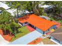An aerial view of a cozy home featuring a vibrant orange roof, set within a lush, tree-lined neighborhood at 2156 Greenbriar Blvd, Clearwater, FL 33763