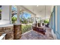 Inviting front porch featuring stone columns, brick floors, and a cozy swing, perfect for relaxing outdoors at 5318 Candler View Dr, Lithia, FL 33547