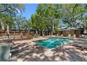 Community pool with a paved deck, lounge chairs, tables, umbrellas and mature shade trees at 1486 Mahogany Ln # 703, Palm Harbor, FL 34683