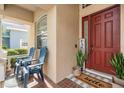 Inviting front porch with brick-patterned flooring, seating, and a charming 'Hello' welcome mat at the red front door at 30817 Pumpkin Ridge Dr, Wesley Chapel, FL 33543