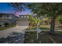 Desirable two-story home featuring a wide driveway, two-car garage, mature trees, and tropical plants at 10636 Dawns Light Dr, Riverview, FL 33578