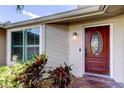View of the wood front door with decorative oval glass, landscaping, and exterior window at 1041 Persimmon Dr, Palm Harbor, FL 34683