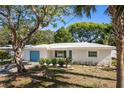 Charming single-story home with a light blue door and one-car garage door complemented by mature trees and landscaping at 1152 Jackmar Rd, Dunedin, FL 34698