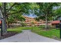 Beautifully landscaped exterior of a beige building with red accents and mature trees at 3062 Eastland Blvd # 402, Clearwater, FL 33761