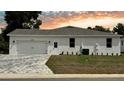 View of exterior showcasing attached two car garage, white stucco, a neatly maintained lawn and interlocking brick driveway at 13532 14Th St, Dade City, FL 33525