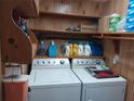 Functional laundry room featuring a washer, dryer, wood paneling, and overhead storage shelves at 8313 Cavalry Dr, Hudson, FL 34667