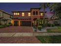 Mediterranean-style home at dusk featuring a brick driveway, two-car garage, and lush landscaping at 2608 Calvano Dr, Land O Lakes, FL 34639