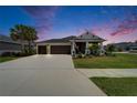 Beautiful single-story home with a three-car garage, landscaped front yard, and a cozy porch, all under a twilight sky at 5828 Clairwood Ct, Palmetto, FL 34221