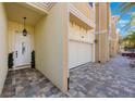Exterior view showing a charming tan townhome featuring a two-car garage and a brick-paved driveway at 789 Grand Cypress Ln, Tarpon Springs, FL 34689