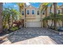 Beautiful tan townhome featuring lush landscaping, palm trees, and a brick-paved driveway at 789 Grand Cypress Ln, Tarpon Springs, FL 34689