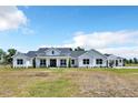 Stunning white farmhouse with black trim, a covered porch, and a large, well-manicured lawn on a sunny day at 14902 Sweat Loop Rd, Wimauma, FL 33598