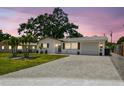 A charming, single-story home with a well-manicured lawn and an elegant brick driveway is pictured at sunset at 2004 Yale Ave, Dunedin, FL 34698