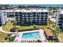 Aerial view of white condo building with pool, lawn, and glimpses of the ocean beyond at 9815 Harrell Ave # 503, Treasure Island, FL 33706