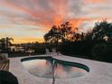 Kidney-shaped swimming pool with patio and lounge chairs, set against a backdrop of a vibrant sunset at 1980 Forked Creek Dr, Englewood, FL 34223