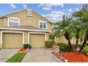 Townhouse featuring attached garage, neutral toned stucco exterior, and tidy landscaping with palm trees at 11162 Kapok Grand Cir, Madeira Beach, FL 33708