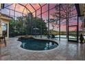 Screened-in pool area with a hot tub, patio furniture, travertine tile, and a view of the lake at sunset at 11817 Glen Wessex Ct, Tampa, FL 33626