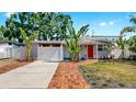 Charming one-story home with a red door, well-manicured lawn, tropical landscaping, and driveway at 4735 W Oklahoma Ave, Tampa, FL 33616