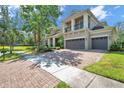 Long brick paved driveway leading up to a tan two-story home with a balcony and three-car garage at 5117 Longspur Ct, Lithia, FL 33547
