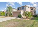 View of a two-story home with a two-car garage, a landscaped front yard with a palm tree, and healthy green grass at 10424 Laguna Plains Dr, Riverview, FL 33578