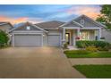 Charming one-story home at dusk featuring a three-car garage and beautifully landscaped front yard with colorful flowers at 4166 Epic Cv, Land O Lakes, FL 34638