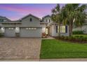 Charming home featuring a three-car garage, well-manicured lawn, and tropical palm trees adding curb appeal at dusk at 19608 Lonesome Pine Dr, Land O Lakes, FL 34638