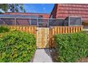 Inviting view of a home's entrance through a wooden gate and fence, surrounded by green bushes at 706 1St Ct, Palm Harbor, FL 34684