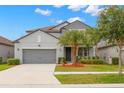 Charming two-story home boasts a well-manicured lawn, gray exterior, complemented by mature palm trees and a two-car garage at 10623 Bahama Woodstar Ct, Riverview, FL 33579